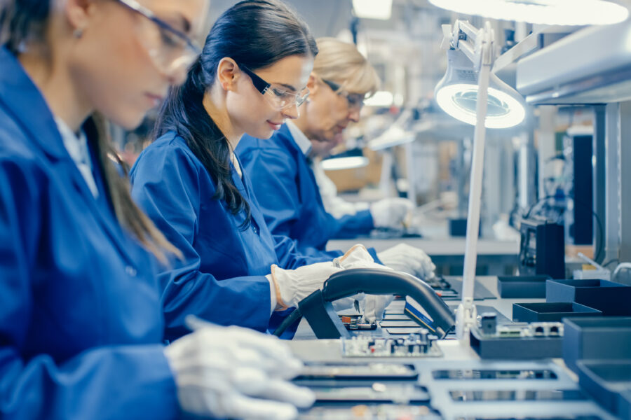 Female Electronics Factory Workers in Blue Work Coat and Protective Glasses Assembling Printed Circuit Boards for Smartphones with Tweezers.