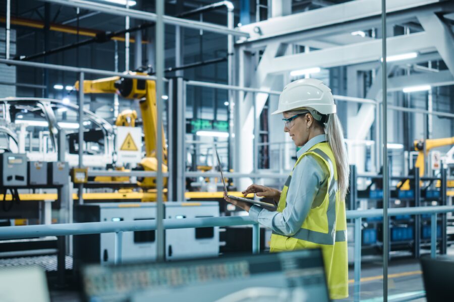 Car Factory: Female Automotive Engineer Wearing Hard Hat, Standing, Using Laptop