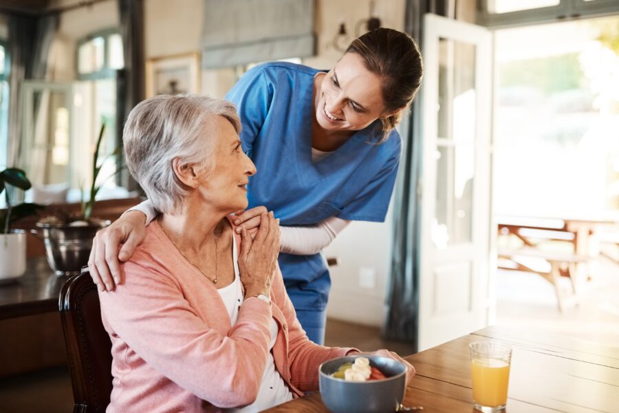 Elderly woman with nurse (caregiver) at her home in living room.