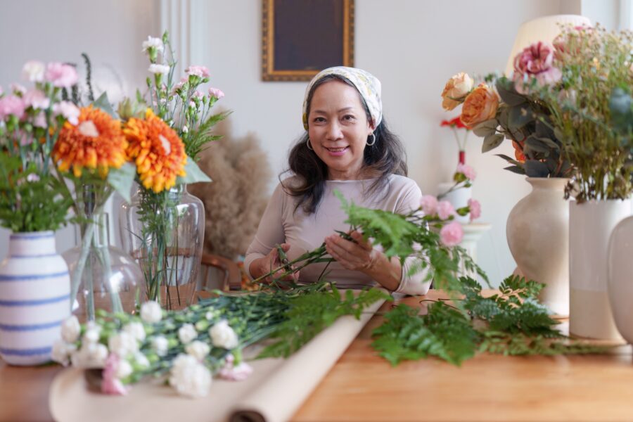 Older East Asian florist, small business owner, putting flowers in a vase