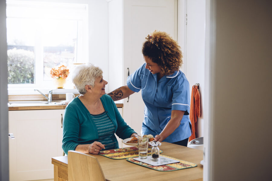 Care worker giving an old lady her dinner in her home.