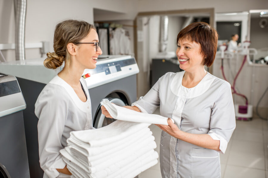 Senior washwoman making up clean towels with young assistant in the hotel laundry