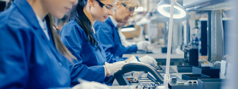 Female Electronics Factory Workers in Blue Work Coat and Protective Glasses Assembling Printed Circuit Boards for Smartphones with Tweezers.